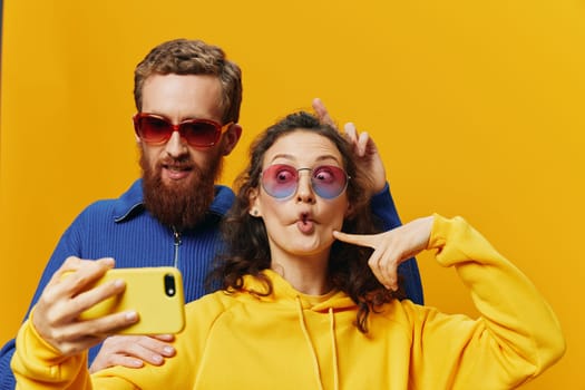 Woman and man funny couple with phones in hand social networking and communication crooked do selfies smile fun, on yellow background. The concept of real family relationships, freelancers, work online. High quality photo