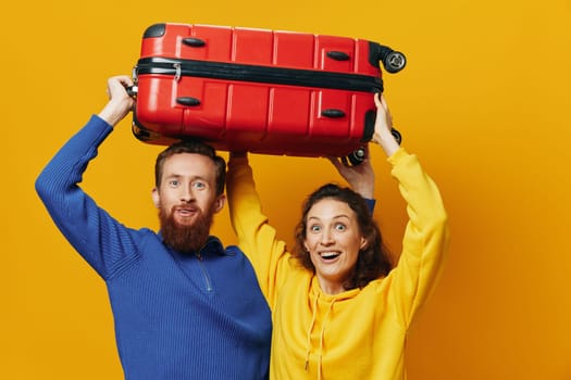 Woman and man smiling, suitcases in hand with yellow and red suitcase smiling merrily and crooked, yellow background, going on a trip, family vacation trip, newlyweds. High quality photo