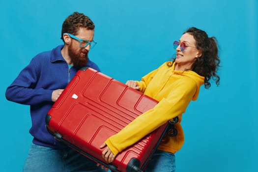 Woman and man smile suitcases in hand with yellow and red suitcase smile fun, on blue background, packing for a trip, family vacation trip. High quality photo