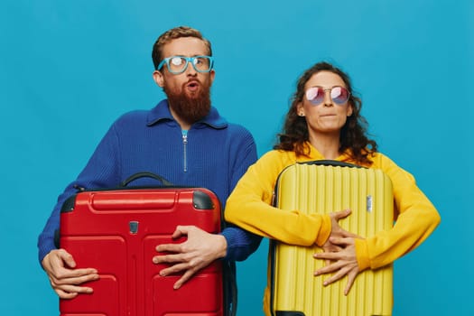 Woman and man smile suitcases in hand with yellow and red suitcase smile fun, on blue background, packing for a trip, family vacation trip. High quality photo