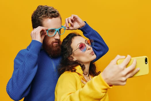 Woman and man funny couple with phones in hand social networking and communication crooked do selfies smile fun, on yellow background. The concept of real family relationships, freelancers, work online. High quality photo