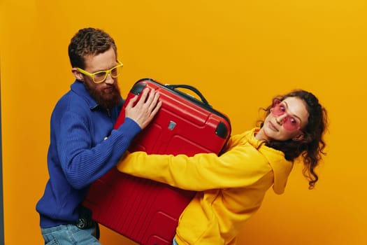 Woman and man smiling, suitcases in hand with yellow and red suitcase smiling merrily and crooked, yellow background, going on a trip, family vacation trip, newlyweds. High quality photo