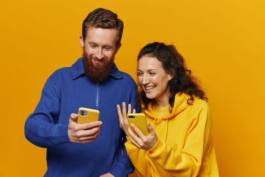 Man and woman couple smiling merrily with phone in hand social media viewing photos and videos, on yellow background, symbols signs and hand gestures, family freelancers. High quality photo