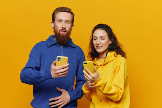 Man and woman couple smiling merrily with phone in hand social media viewing photos and videos, on yellow background, symbols signs and hand gestures, family freelancers. High quality photo