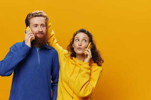 Woman and man cheerful couple with phones in hand talking on cell phone crooked smile cheerful, on yellow background. The concept of real family relationships, talking on the phone, work online. High quality photo