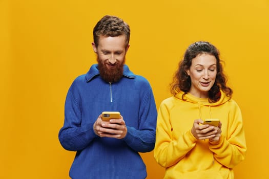 Woman and man cheerful couple with phones in hand social networking and communication crooked smile fun and fight, in yellow background. The concept of real family relationships, freelancers, work online. High quality photo