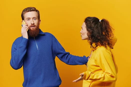 Man and woman couple with phone in hand call talking on the phone, on a yellow background, symbols signs and hand gestures, family quarrel jealousy and scandal. High quality photo