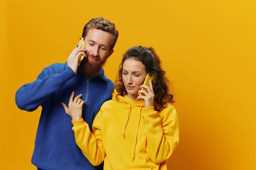 Woman and man cheerful couple with phones in hand talking on cell phone crooked smile cheerful, on yellow background. The concept of real family relationships, talking on the phone, work online. High quality photo