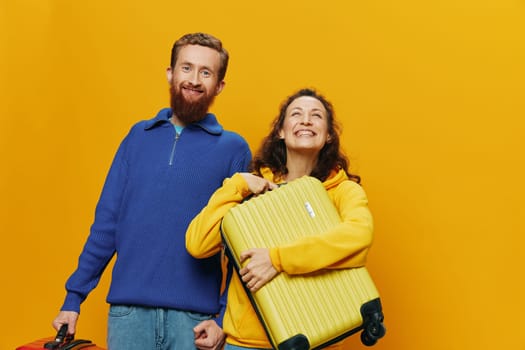 Woman and man smiling, suitcases in hand with yellow and red suitcase smiling merrily and crooked, yellow background, going on a trip, family vacation trip, newlyweds. High quality photo