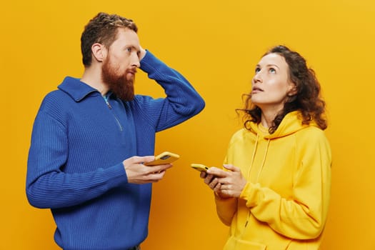 Woman and man cheerful couple with phones in hand social networking and communication crooked smile fun and fight, in yellow background. The concept of real family relationships, freelancers, work online. High quality photo