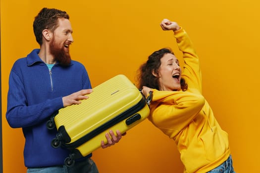 Woman and man smiling, suitcases in hand with yellow and red suitcase smiling merrily and crooked, yellow background, going on a trip, family vacation trip, newlyweds. High quality photo