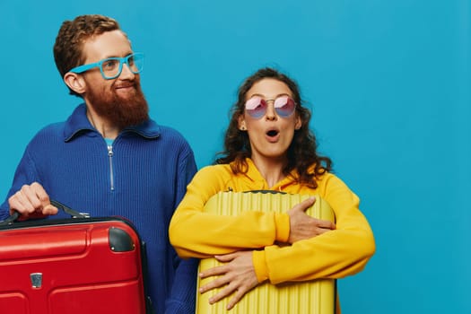 Woman and man smile suitcases in hand with yellow and red suitcase smile fun, on blue background, packing for a trip, family vacation trip. High quality photo