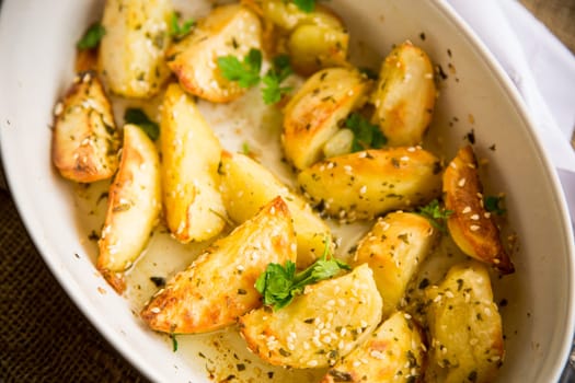 potatoes baked with sesame seeds, herbs and spices in the oven in a ceramic form.