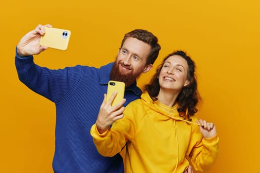 Man and woman couple smiling merrily with phone in hand social media viewing photos and videos, on yellow background, symbols signs and hand gestures, family freelancers. High quality photo