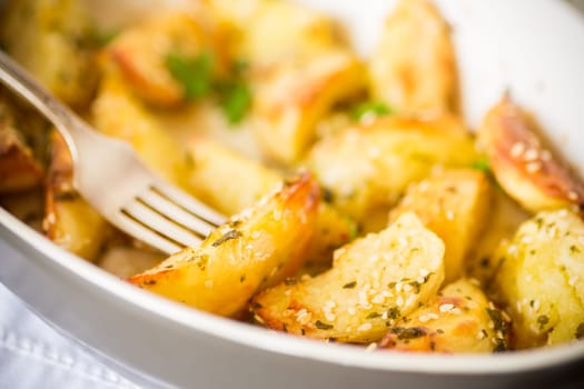 potatoes baked with sesame seeds, herbs and spices in the oven in a ceramic form.
