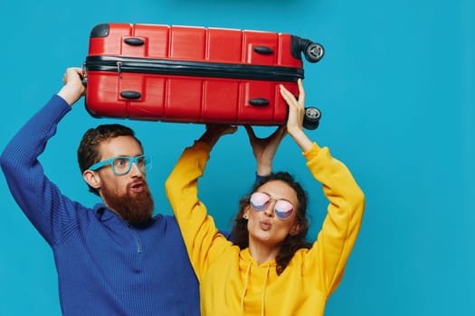 Woman and man smile suitcases in hand with yellow and red suitcase smile fun, on blue background, packing for a trip, family vacation trip. High quality photo