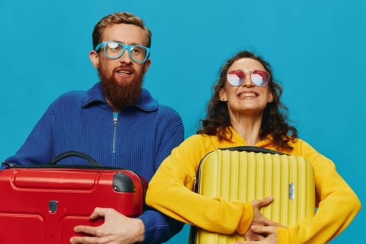 Woman and man smile suitcases in hand with yellow and red suitcase smile fun, on blue background, packing for a trip, family vacation trip. High quality photo