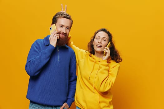 Woman and man cheerful couple with phones in hand talking on cell phone crooked smile cheerful, on yellow background. The concept of real family relationships, talking on the phone, work online. High quality photo