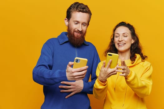 Man and woman couple smiling merrily with phone in hand social media viewing photos and videos, on yellow background, symbols signs and hand gestures, family freelancers. High quality photo