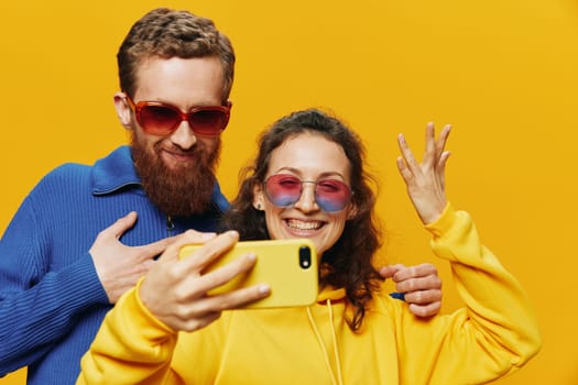 Woman and man funny couple with phones in hand social networking and communication crooked do selfies smile fun, on yellow background. The concept of real family relationships, freelancers, work online. High quality photo