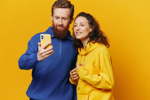 Man and woman couple smiling merrily with phone in hand social media viewing photos and videos, on yellow background, symbols signs and hand gestures, family freelancers. High quality photo