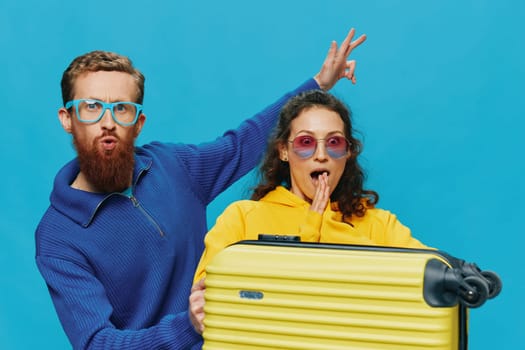 Woman and man smile sitting on suitcase with yellow suitcase smile, on blue background, packing for trip, family vacation trip. High quality photo