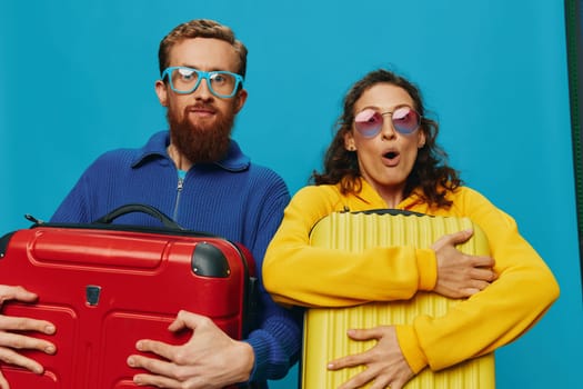 Woman and man smile suitcases in hand with yellow and red suitcase smile fun, on blue background, packing for a trip, family vacation trip. High quality photo