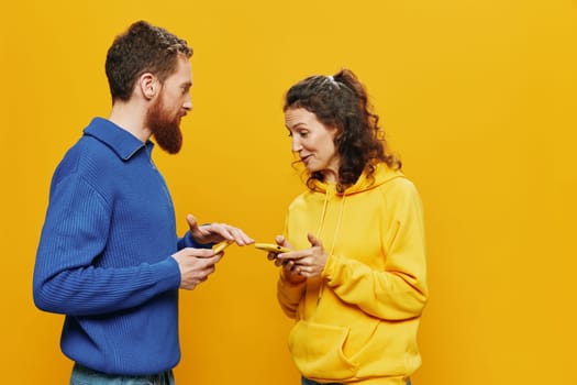 Woman and man cheerful couple with phones in hand social networking and communication crooked smile fun and fight, in yellow background. The concept of real family relationships, freelancers, work online. High quality photo