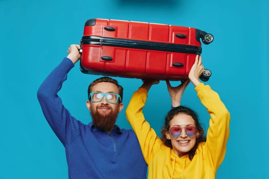 Woman and man smile suitcases in hand with yellow and red suitcase smile fun, on blue background, packing for a trip, family vacation trip. High quality photo