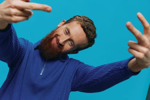 Portrait of a man in a sweater smile and happiness, hand signs and symbols, on a blue background. Lifestyle positive, copy place. High quality photo