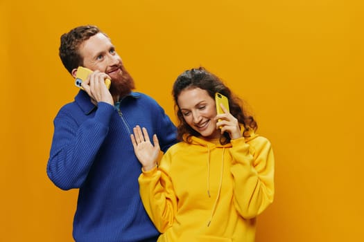 Man and woman couple smiling merrily with phone in hand social media viewing photos and videos, on yellow background, symbols signs and hand gestures, family freelancers. High quality photo