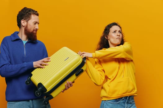 Woman and man smiling, suitcases in hand with yellow and red suitcase smiling merrily and crooked, yellow background, going on a trip, family vacation trip, newlyweds. High quality photo