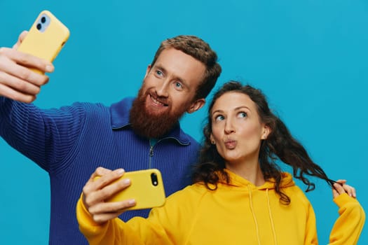 Woman and man funny couple with phones in hand taking selfies crooked smile fun, on blue background. The concept of real family relationships, talking on the phone, work online. High quality photo