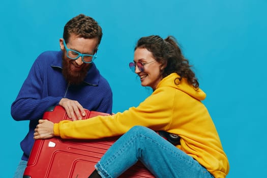 Woman and man smile suitcases in hand with yellow and red suitcase smile fun, on blue background, packing for a trip, family vacation trip. High quality photo