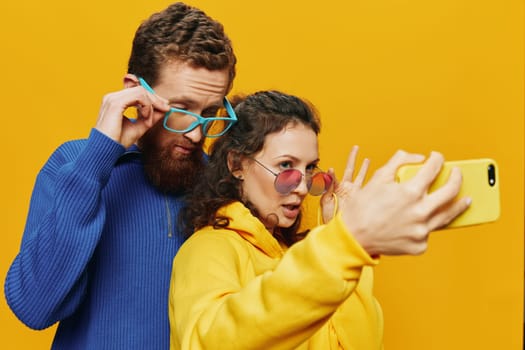 Woman and man funny couple with phones in hand social networking and communication crooked do selfies smile fun, on yellow background. The concept of real family relationships, freelancers, work online. High quality photo