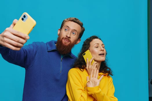 Woman and man funny couple with phones in hand taking selfies crooked smile fun, on blue background. The concept of real family relationships, talking on the phone, work online. High quality photo