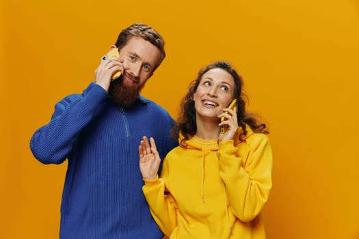 Woman and man cheerful couple with phones in hand talking on cell phone crooked smile cheerful, on yellow background. The concept of real family relationships, talking on the phone, work online. High quality photo