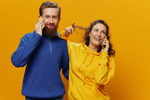 Woman and man cheerful couple with phones in hand talking on cell phone crooked smile cheerful, on yellow background. The concept of real family relationships, talking on the phone, work online. High quality photo