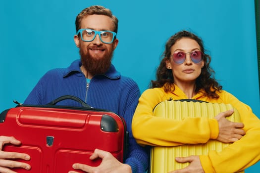 Woman and man smile suitcases in hand with yellow and red suitcase smile fun, on blue background, packing for a trip, family vacation trip. High quality photo