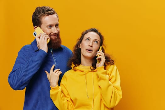 Man and woman couple smiling merrily with phone in hand social media viewing photos and videos, on yellow background, symbols signs and hand gestures, family freelancers. High quality photo