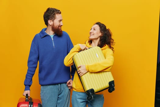 Woman and man smiling, suitcases in hand with yellow and red suitcase smiling merrily and crooked, yellow background, going on a trip, family vacation trip, newlyweds. High quality photo