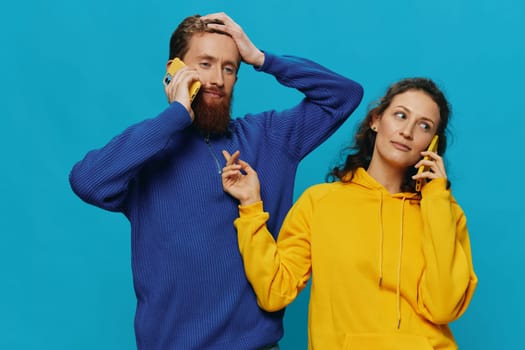 Woman and man cheerful couple with phones in their hands crooked smile cheerful, on blue background. The concept of real family relationships, talking on the phone, work online. High quality photo