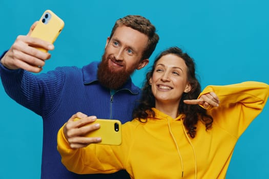 Woman and man funny couple with phones in hand taking selfies crooked smile fun, on blue background. The concept of real family relationships, talking on the phone, work online. High quality photo