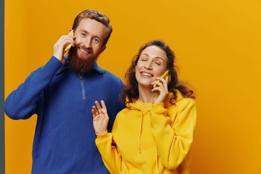 Woman and man cheerful couple with phones in hand talking on cell phone crooked smile cheerful, on yellow background. The concept of real family relationships, talking on the phone, work online. High quality photo