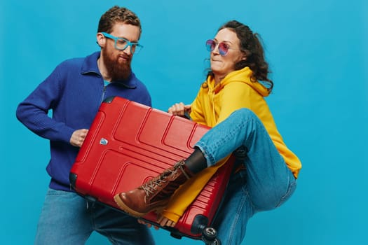 Woman and man smile suitcases in hand with yellow and red suitcase smile fun, on blue background, packing for a trip, family vacation trip. High quality photo