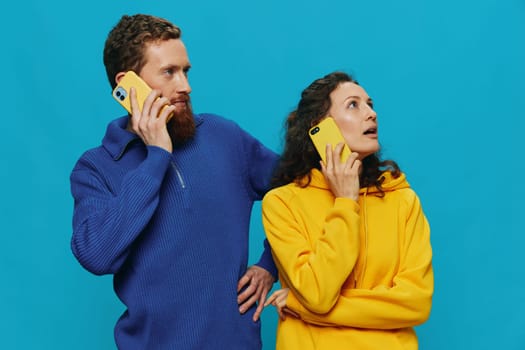 Woman and man cheerful couple with phones in their hands crooked smile cheerful, on blue background. The concept of real family relationships, talking on the phone, work online. High quality photo