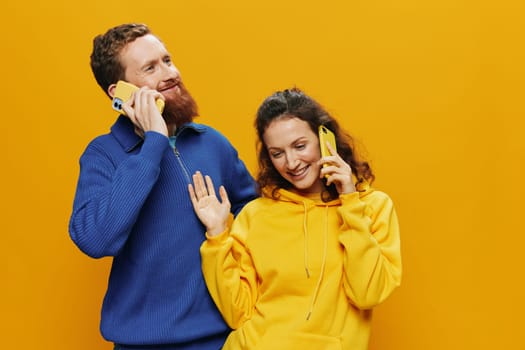 Man and woman couple smiling merrily with phone in hand social media viewing photos and videos, on yellow background, symbols signs and hand gestures, family freelancers. High quality photo