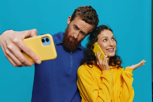 Woman and man funny couple with phones in hand taking selfies crooked smile fun, on blue background. The concept of real family relationships, talking on the phone, work online. High quality photo