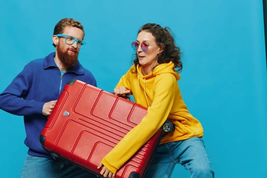 Woman and man smile suitcases in hand with yellow and red suitcase smile fun, on blue background, packing for a trip, family vacation trip. High quality photo