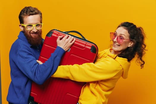 Woman and man smiling, suitcases in hand with yellow and red suitcase smiling merrily and crooked, yellow background, going on a trip, family vacation trip, newlyweds. High quality photo